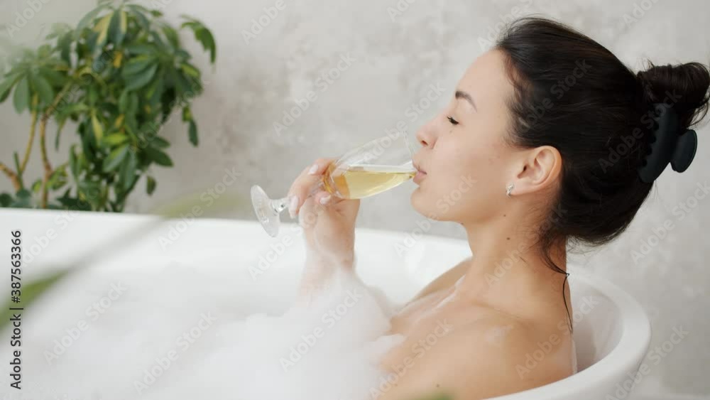 Slow motion of happy girl enjoying champage in warm bath smiling relaxing at home in bathroom. Alcoholic drinks and youth lifestyle concept. Slow motion of happy girl enjoying champage in warm bath smiling relaxing at home in bathroom. Alcoholic drinks and youth lifestyle concept.