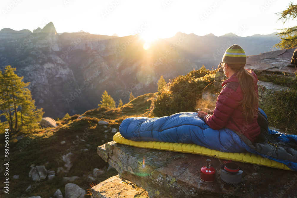 A woman enjoying breakfast from her bivouac on a beautiful morning in the mountains. - obrazy, fototapety, plakaty 
