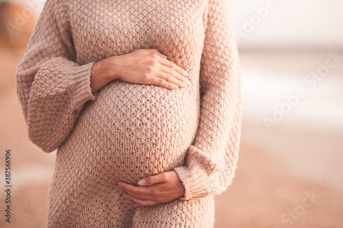 Pregnant woman wearing cozy knitted sweater holding tummy with hands outdoors close up. Motherhood. Maternity. Heathy lifestyle.