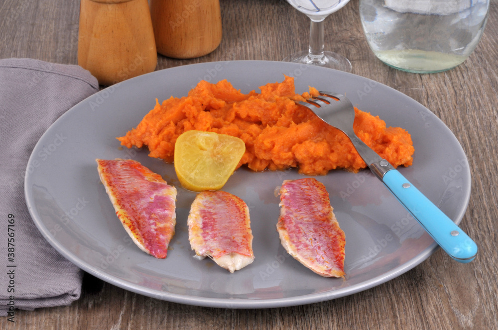 Filets de rouget dans une assiette avec une rondelle de citron et de la purée de carottes en gros plan