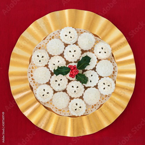 Festive home made Christmas mince pies on a gold plate with holly on a red tablecloth background. Xmas food composition. Flat lay, top view.