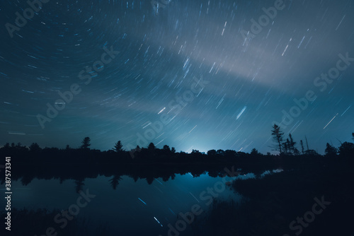 Nearly clear night skies as seen from Torrance Barrens dark sky reserve, Muskoka, Ontario, featuring star trails, lake, reflection and a little cloud