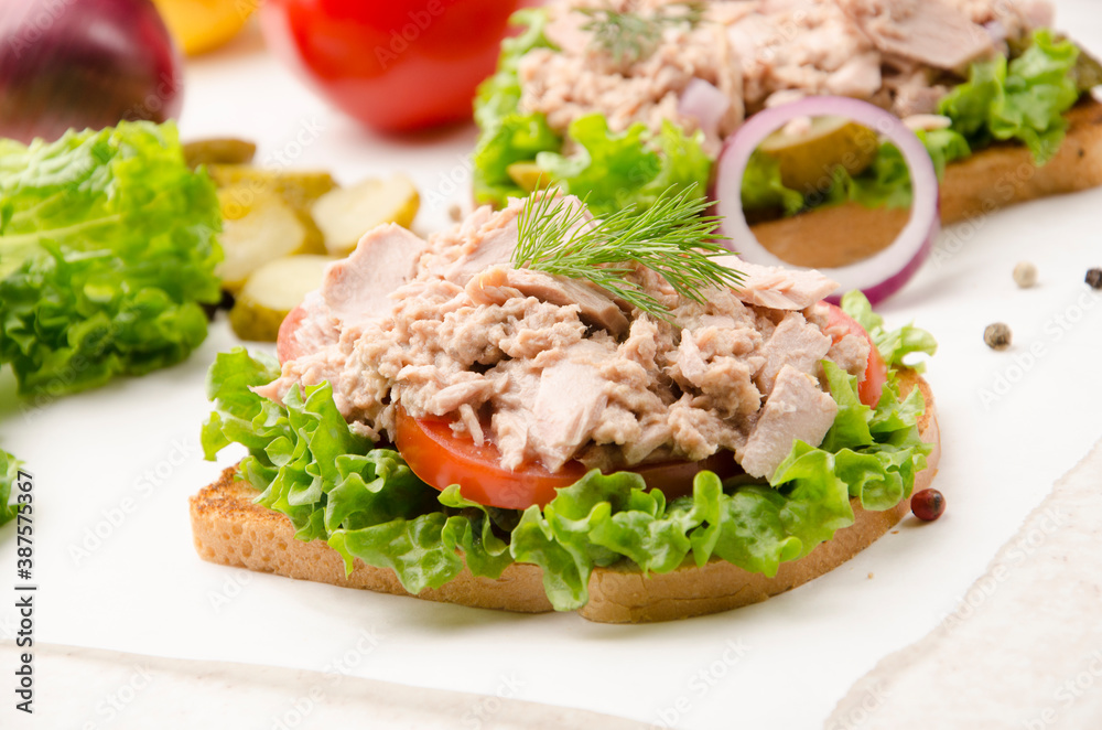 Tuna sandwiches with lettuce tomatoes and onions on parchment paper
