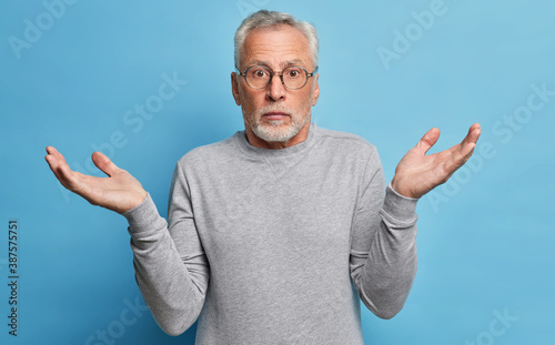 Questioned puzzled grey haired man spreads hands in clueless gesture shrugs shoulders has to make choice dressed in casual clothes cannot understand whats wrong looks with perplexed expression