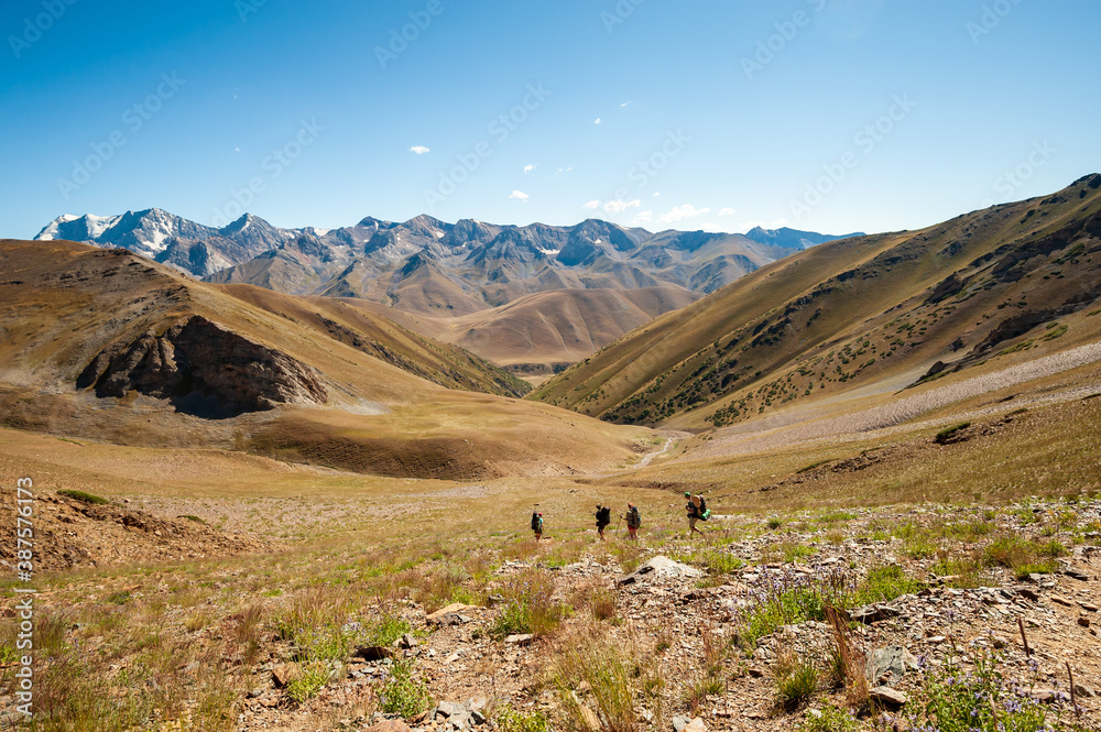 Group of trekkers descending rocky pass with mountain top wiews in high mountains. Young men and women hiking near Sary Chelek lake, Sary-Chelek Jalal Abad region, Kyrgyzstan, Trekking in Central Asia