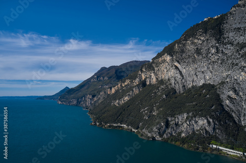Aerial view of the big rocks of Lake Garda, Italy. Red rocks on a blue background. Gray rocky slopes in the water. Alps part on blue sky. Rough rocky stones.