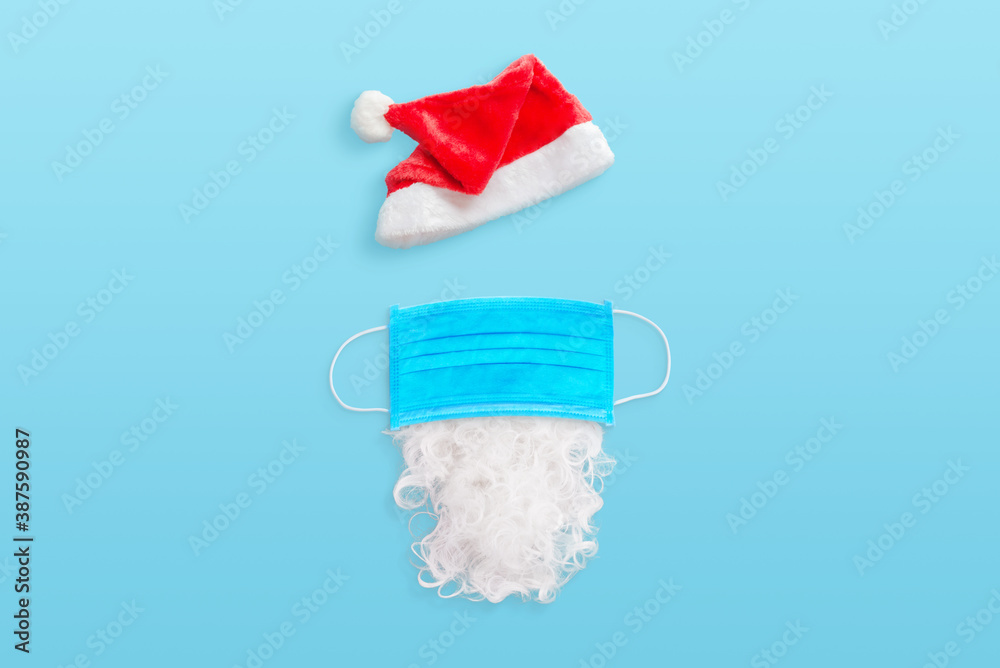 Santa Claus equipment in the coronavirus epidemic concept. Hat, mask and beard on blue desk Santa Claus equipment in the coronavirus epidemic concept. Hat, mask and beard on blue desk