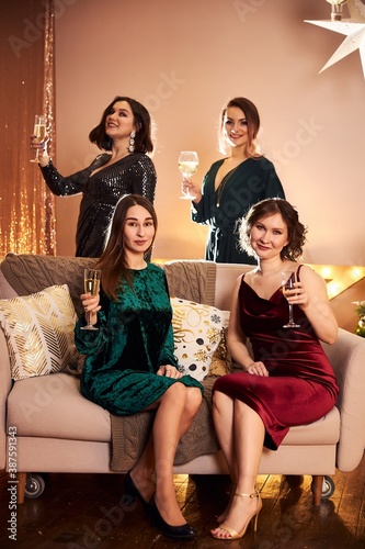 Four beautiful women celebrate the new year or Christmas in beautiful evening dresses in a decorated for the holiday room with garlands and gifts drink at the party
