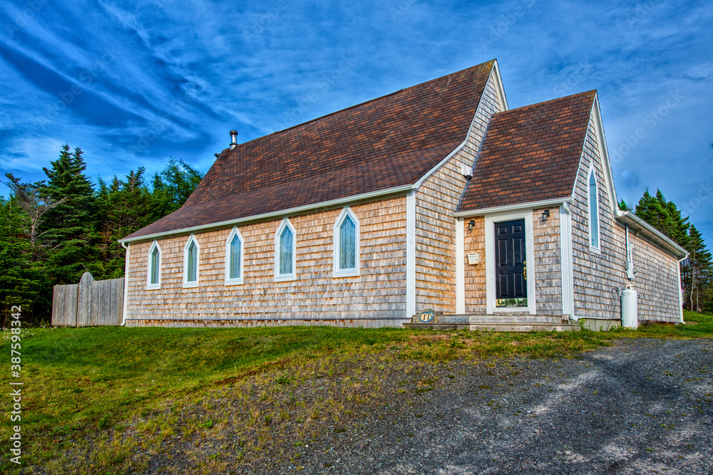 A vintage church recently renovated with cedar shake siding, brown roof shingles and five clear glass steeple clerestory windows. There's green grass in the foreground and blue sky in the background.