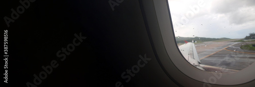 Wide banner, dark background with place for text. Light from the window, airplane porthole, view from the cabin. Raindrops on glass, airfield runway view through the window of plane. Graphic template © Oxana