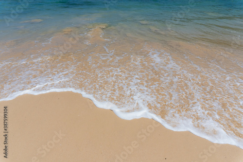 The white little bubble waves hit the sand shore on the beach, background with the clear blue sky on in island