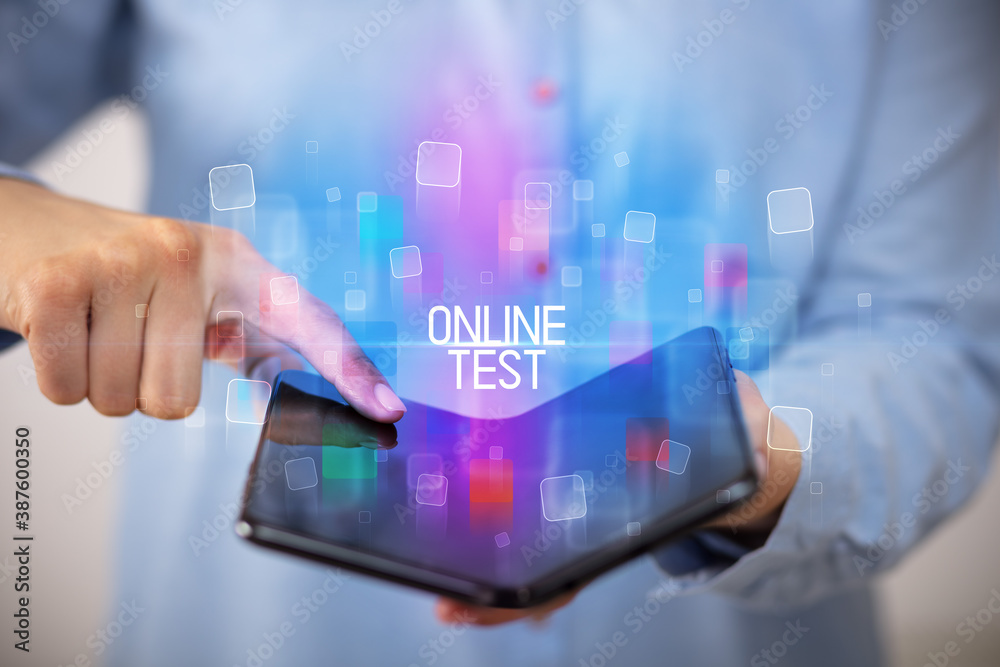 Young man holding a foldable smartphone with ONLINE TEST inscription, educational concept Young man holding a foldable smartphone with ONLINE TEST inscription, educational concept