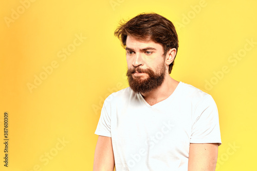 Bearded man in a white T-shirt gestures with his hands emotions studio yellow background
