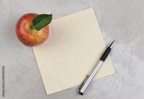 An apple, pen, and napkin on a gray mottled surface. Room for copy or doodle on the napkin.