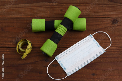 A set of dumbbells a tape measure and COVID-19 mask on a rustic woot surface. Fitness and Safety Concept.