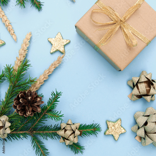 Christmas gift on a sky-blue background with coniferous branches and Christmas toys. New year's background with gold ornaments with bows, cones, wheat spikelets and stars. © Елена Труфанова