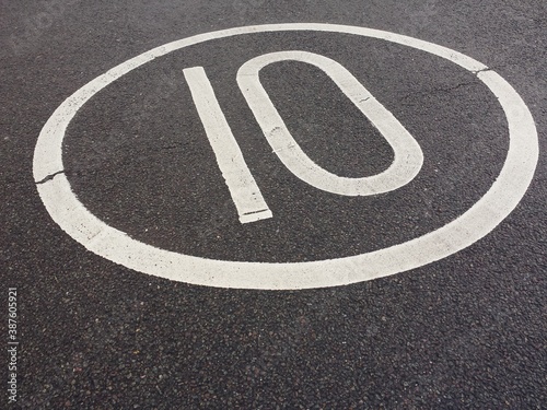 maximum speed limit 10 mph white road sign painted onto textured grey asphalt 