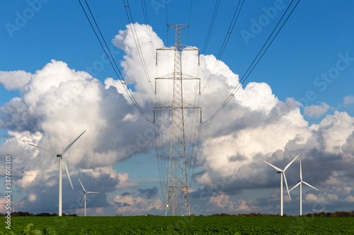 high-voltage power line tower and wind generators in a green field and with a beautiful cloudy blue sky