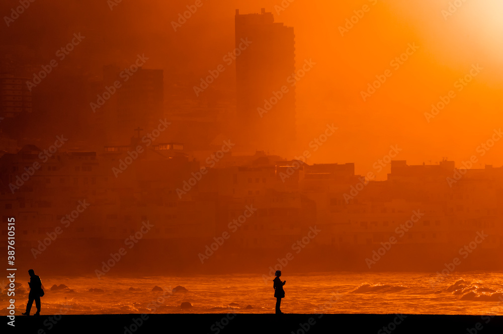 Fototapeta premium Menschen auf dem Kai am Meer mit Handy im Sonnenuntergang
