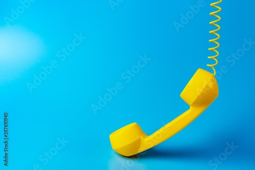 Yellow retro telephone receiver on blue background.