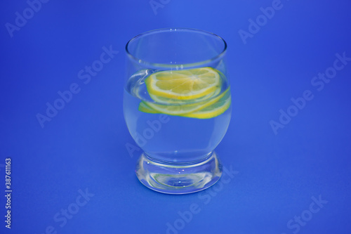 Sliced lemon in a glass of water on an isolated blue background.