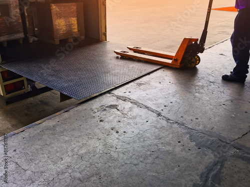 Worker driving forklift loading shipment carton boxes goods on wooden pallet at loading dock from container truck to warehouse cargo storage in freight logistics, transportation industrial, delivery