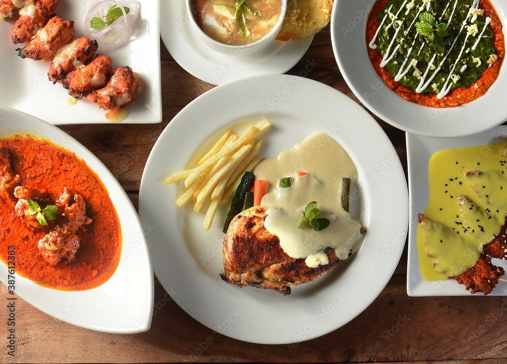 Assorted indian food on wooden background. Dishes and appetizers of indian cuisine. chicken tikka, french fries, chicken soup, palak paneer , mutton rogan josh, chicken strips Assorted indian food on wooden background. Dishes and appetizers of indian cuisine. chicken tikka, french fries, chicken soup, palak paneer , mutton rogan josh, chicken strips