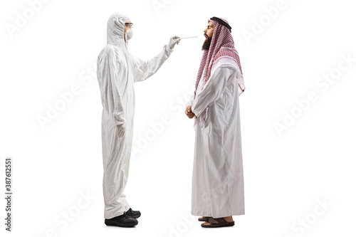 Full length profile shot of an epidemiologist in a hazmat suit taking a cotton swab test from an arab man