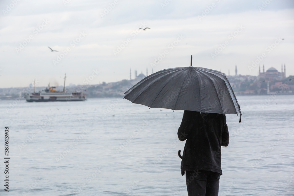 Man standing by the sea with black umbrella on a rainy day