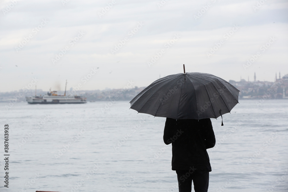 Man standing by the sea with black umbrella on a rainy day