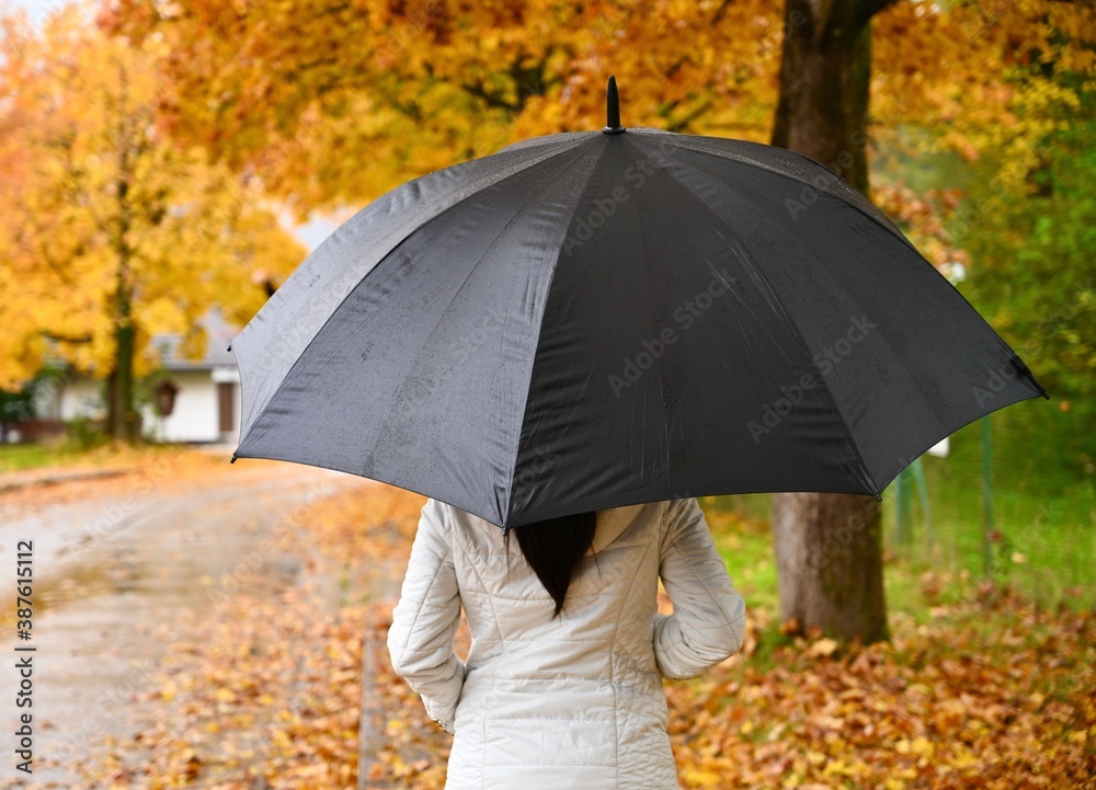 Young woman with black umbrella walking in the rain. autumn rainy day.