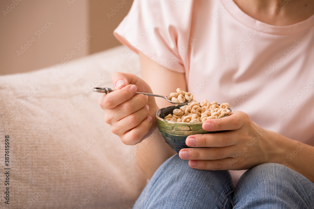 A young girl in jeans and a pink sweater holds a beautiful spoon and a bowl of organic yogurt sprinkled with cereals. The woman is sitting on the couch. Healthy eating A young girl in jeans and a pink sweater holds a beautiful spoon and a bowl of organic yogurt sprinkled with cereals. The woman is sitting on the couch. Healthy eating