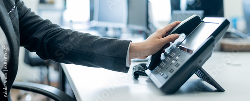 Close-up of a female employee's hand on a landline phone. Woman picks up a push-button telephone at the workplace in the office
