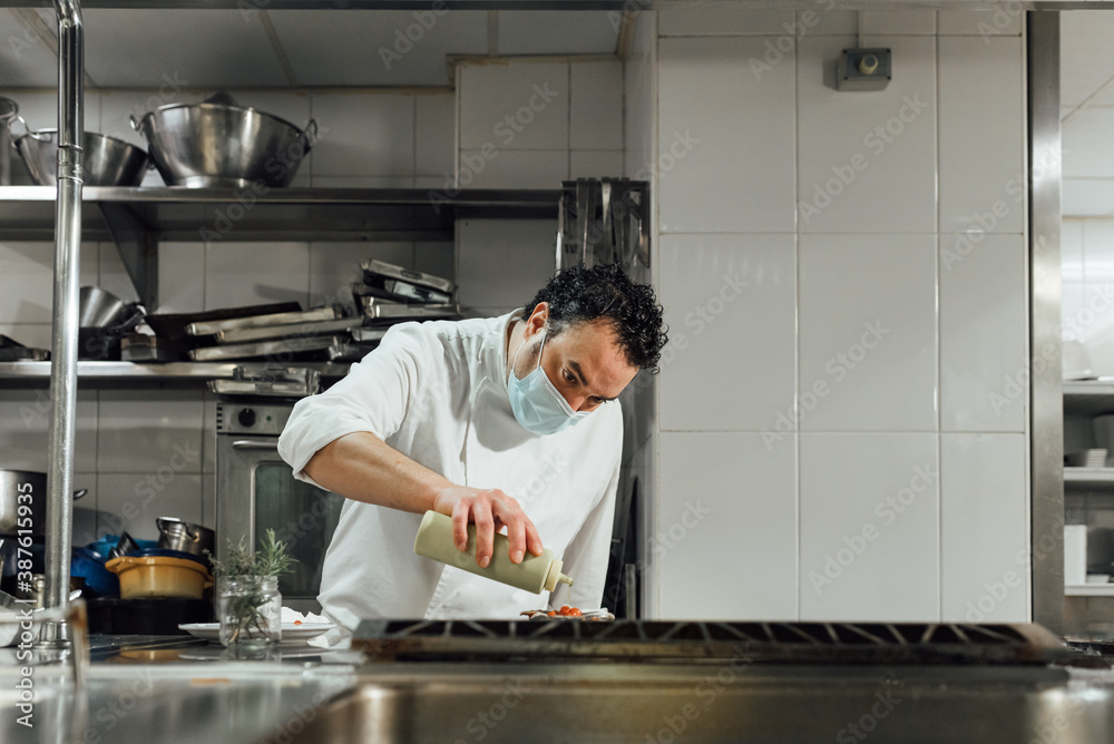 The masked chef preparing a dish of food in the kitchen ready to be served. The masked chef preparing a dish of food in the kitchen ready to be served.