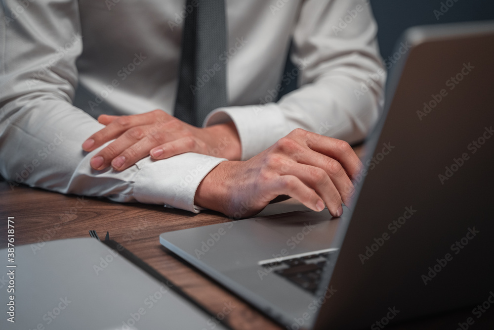 Businessman in white shirt and gray tie in front of a laptop on a wooden desk with items Businessman in white shirt and gray tie in front of a laptop on a wooden desk with items