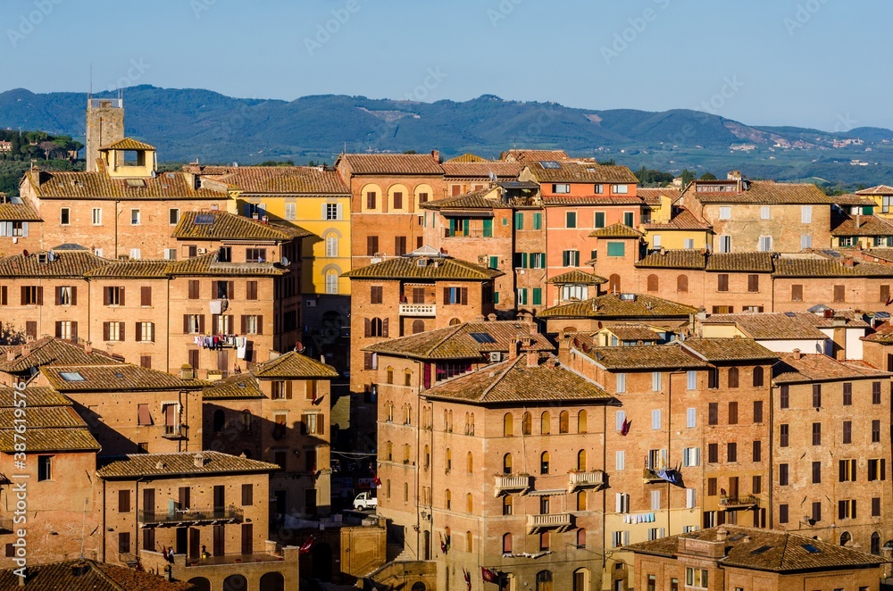 City scape of Siena, the medieval town on the hill with red brick tower, houses and roofs under the blue sky in Tuscany, Italy.