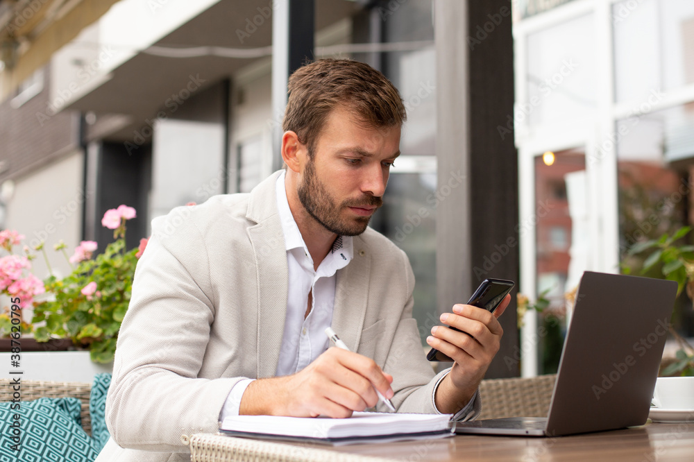 The young businessman is working online, and writing in his notebook in the coffee bar The young businessman is working online, and writing in his notebook in the coffee bar