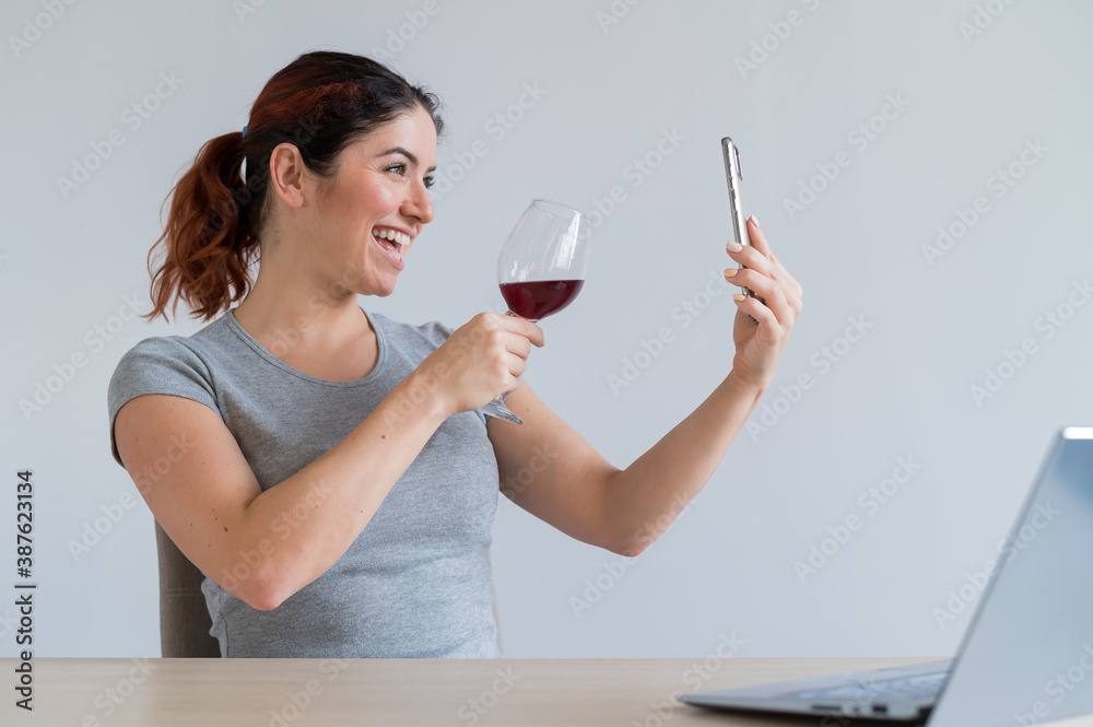 Caucasian woman drinks red wine and communicates with friends via video communication on a smartphone. The quarantined girl celebrates the holiday via an online conference Caucasian woman drinks red wine and communicates with friends via video communication on a smartphone. The quarantined girl celebrates the holiday via an online conference