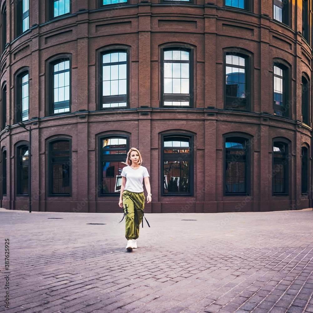 Girl in hip hop clothes walking in front of curved brick building in the city in a post industrial urban environment