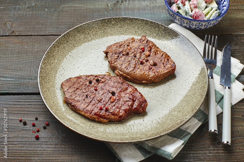 Two grilled ribeye steaks, spices and tomato-cucumber salad with sour cream