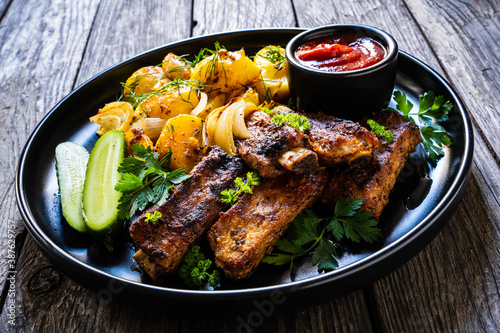 Tasty roasted ribs with baked potatoes vegetables on wooden table