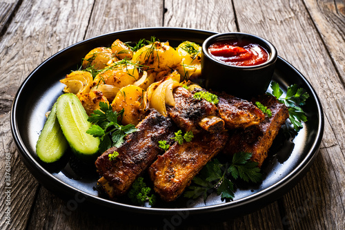 Tasty roasted ribs with baked potatoes vegetables on wooden table
