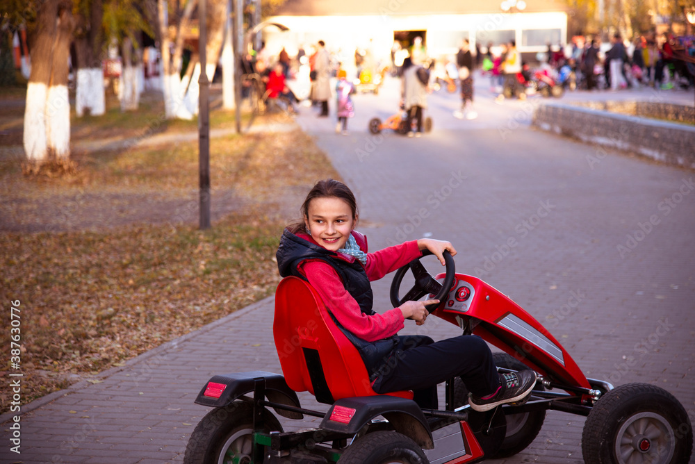 Smiling girl rides children's racing cars in the Park.