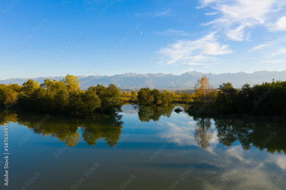 Lake at the edge of the mountains with forest reflected in the clear water. Idyllic autumn landscape. The forest and the sky in the reflection of the water. Quiet autumn fishing landscape