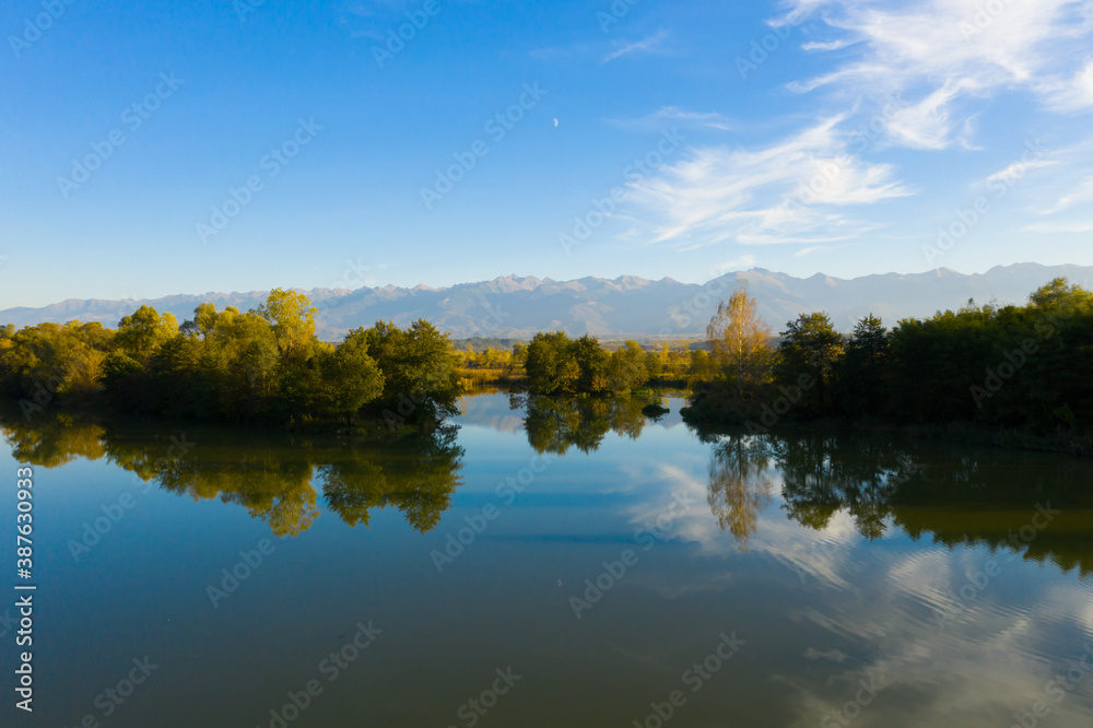 Lake at the edge of the mountains with forest reflected in the clear water. Idyllic autumn landscape. The forest and the sky in the reflection of the water. Quiet autumn fishing landscape