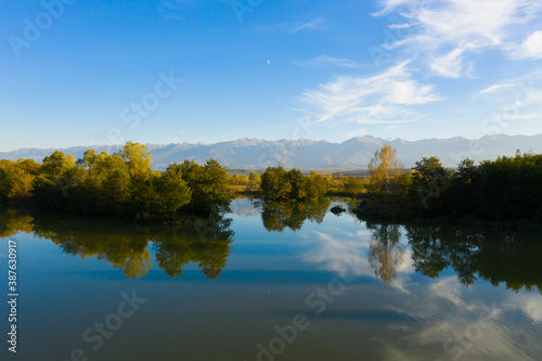 Lake at the edge of the mountains with forest reflected in the clear water. Idyllic autumn landscape. The forest and the sky in the reflection of the water. Quiet autumn fishing landscape