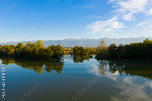 Lake at the edge of the mountains with forest reflected in the clear water. Idyllic autumn landscape. The forest and the sky in the reflection of the water. Quiet autumn fishing landscape © Epic Vision