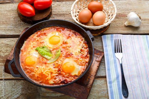 israeli fried eggs shakshuka with cheese in a frying pan next to a fork and a napkin.