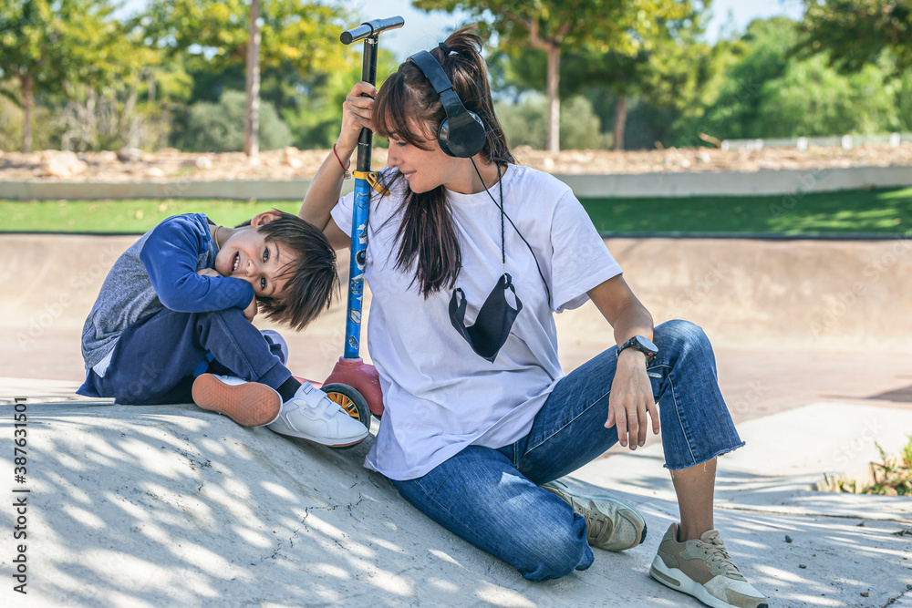 mother and son sitting on the ramp of a skate park in a very affectionate way next to the child's scooter mother and son sitting on the ramp of a skate park in a very affectionate way next to the child's scooter