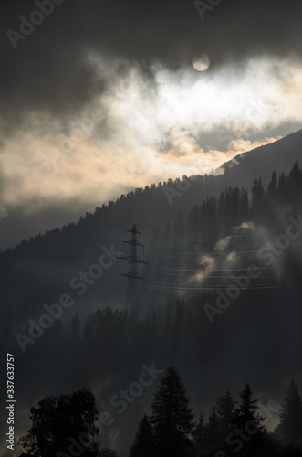 Power line pylon of power grid in misty forest with fog on a beautiful morning in the Swiss alps.